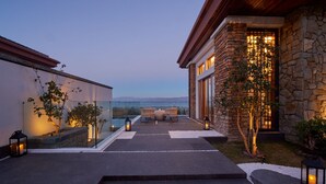 Un patio moderno al aire libre con vista al mar, muros de piedra y una zona de estar con cojines.