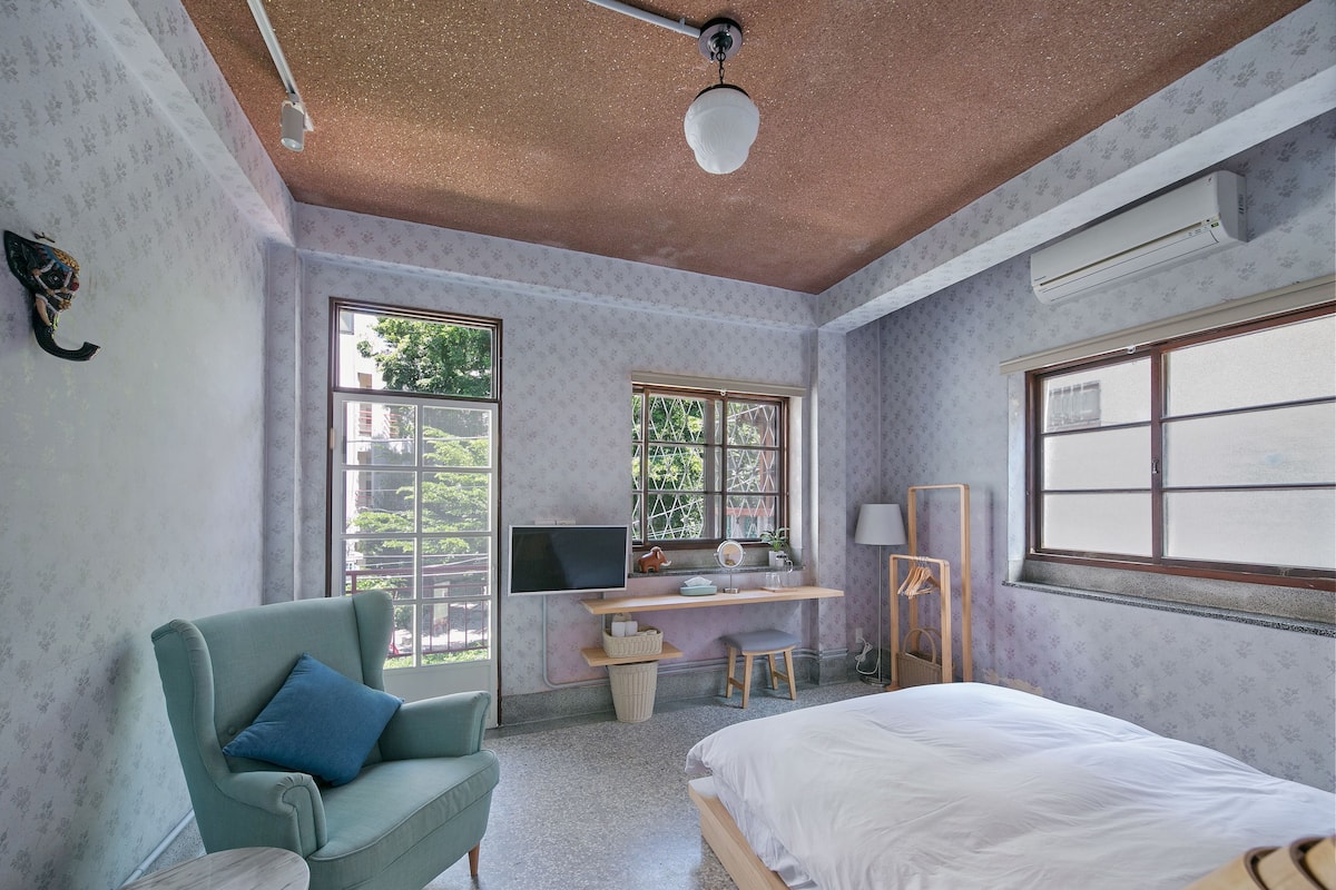 A bedroom with a bed, a desk, a chair, a small table, and a ceiling fan.
