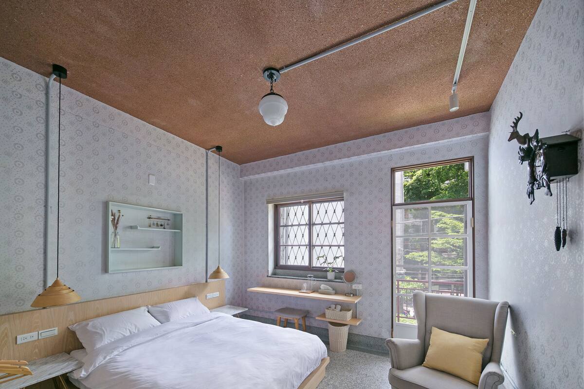 A bedroom with a bed, a desk, a chair, a small table, a window with a view, and a ceiling fan.