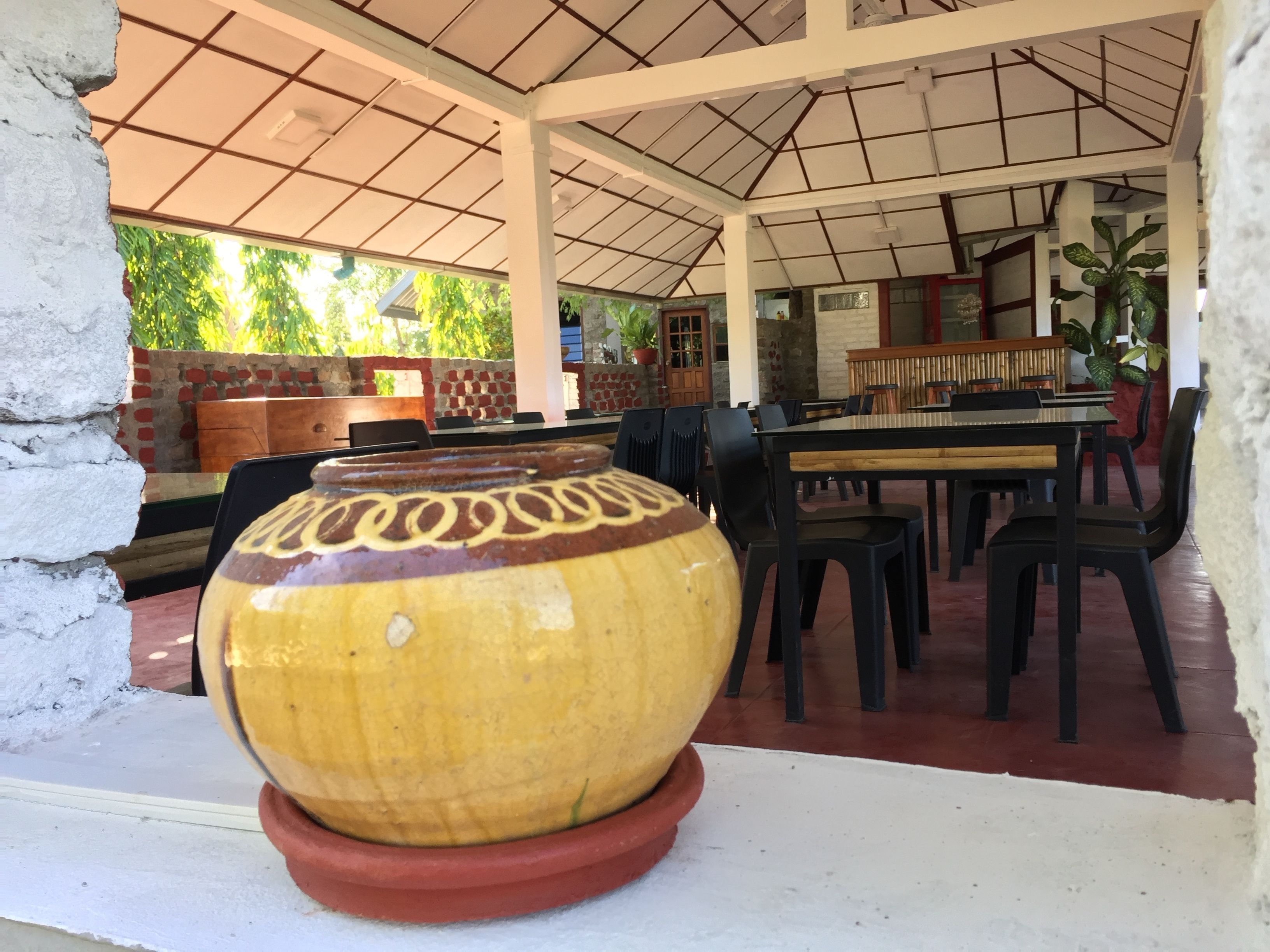 Un restaurante con techo de azulejos, mesas al aire libre y una maceta decorativa en primer plano.