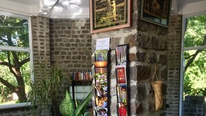 A room with a stone wall, a bookshelf, a large potted plant, and a wicker chair. - Lei Thar Gone Guest House (Yenangyaung)
