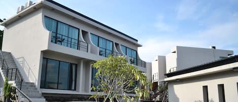 A modern two-story building with large windows, a staircase, and a small tree in the foreground.