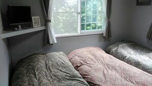 Un dormitorio con dos camas, un televisor en un estante y una ventana con cortinas.