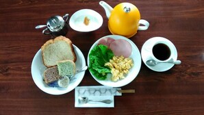 Un desayuno con pan, huevos, jamón y una tetera sobre una mesa de madera.