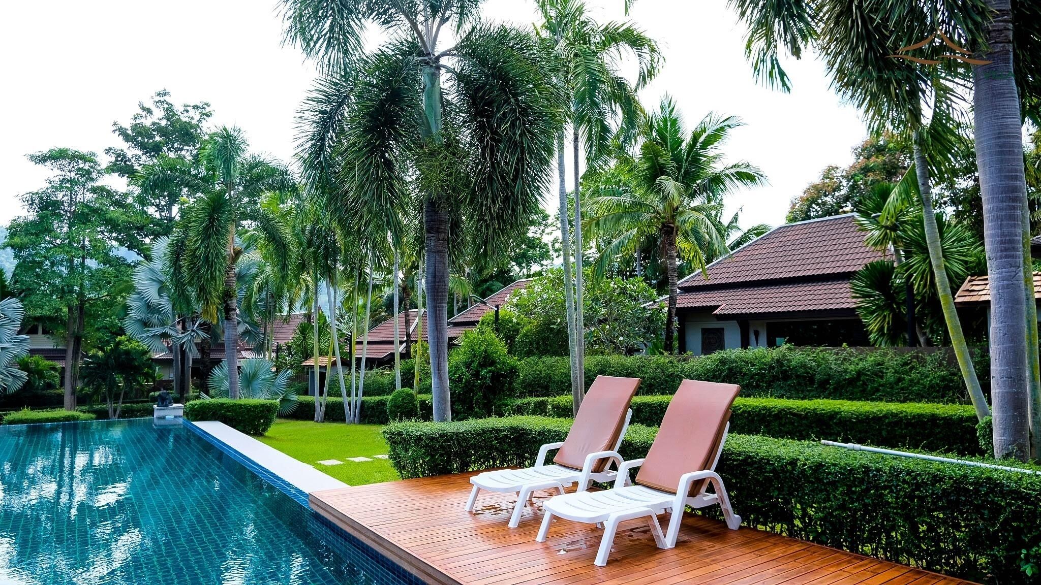A poolside area with two lounge chairs, a wooden deck, and a clear blue pool.