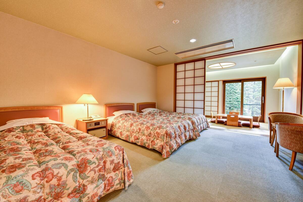 Quarto de hotel com duas camas, área de estar e vista, e portas corrediças tradicionais japonesas.