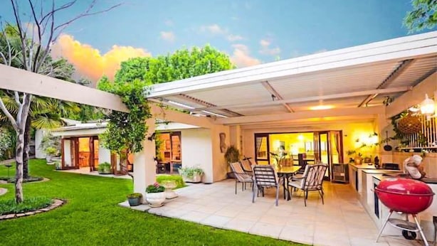A modern house with a covered patio, a barbecue area, and a well-maintained garden. - Noraclox Riverclub (Sandton)