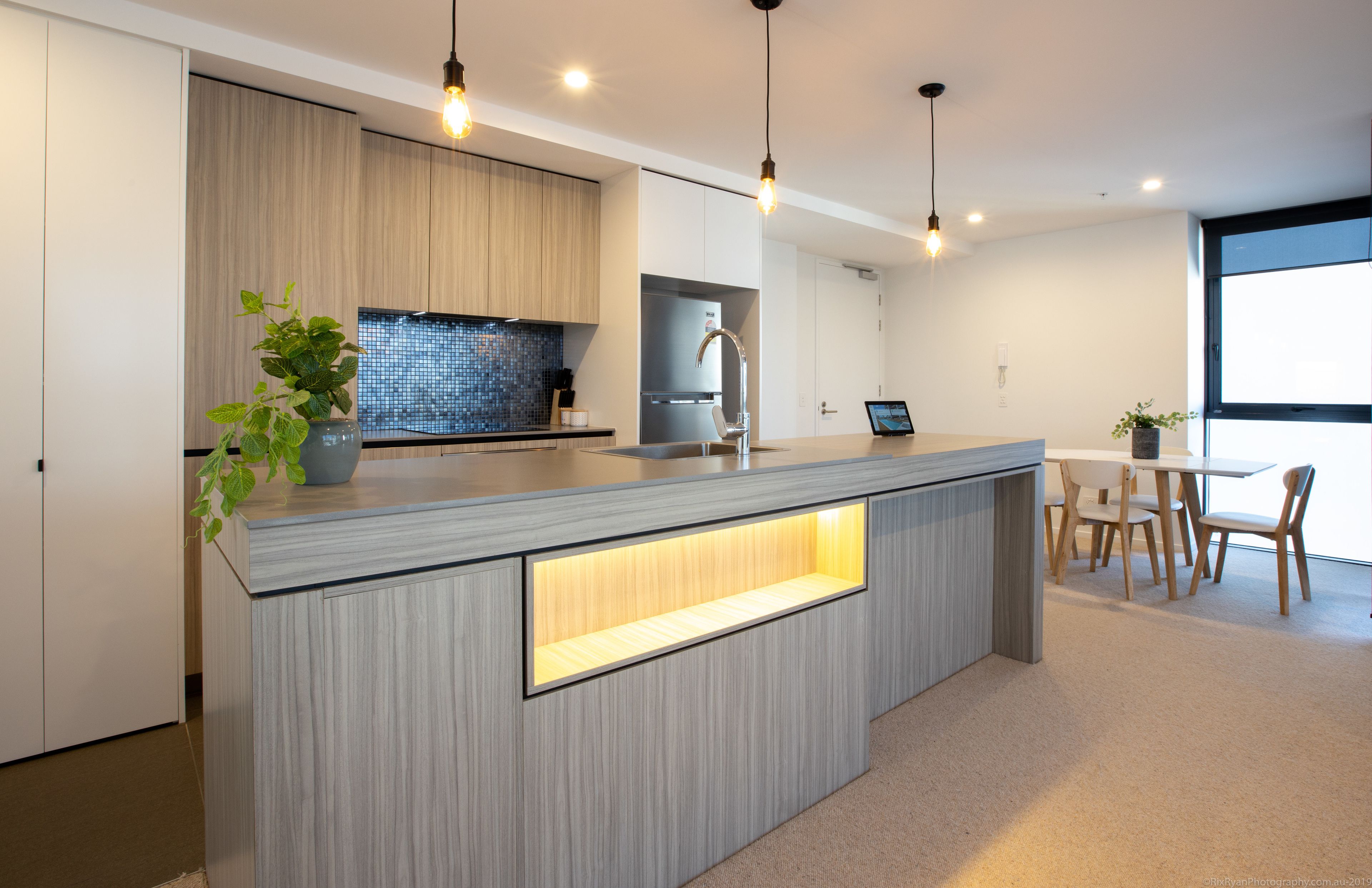 A modern kitchen with a central island, wooden cabinetry, and pendant lighting.