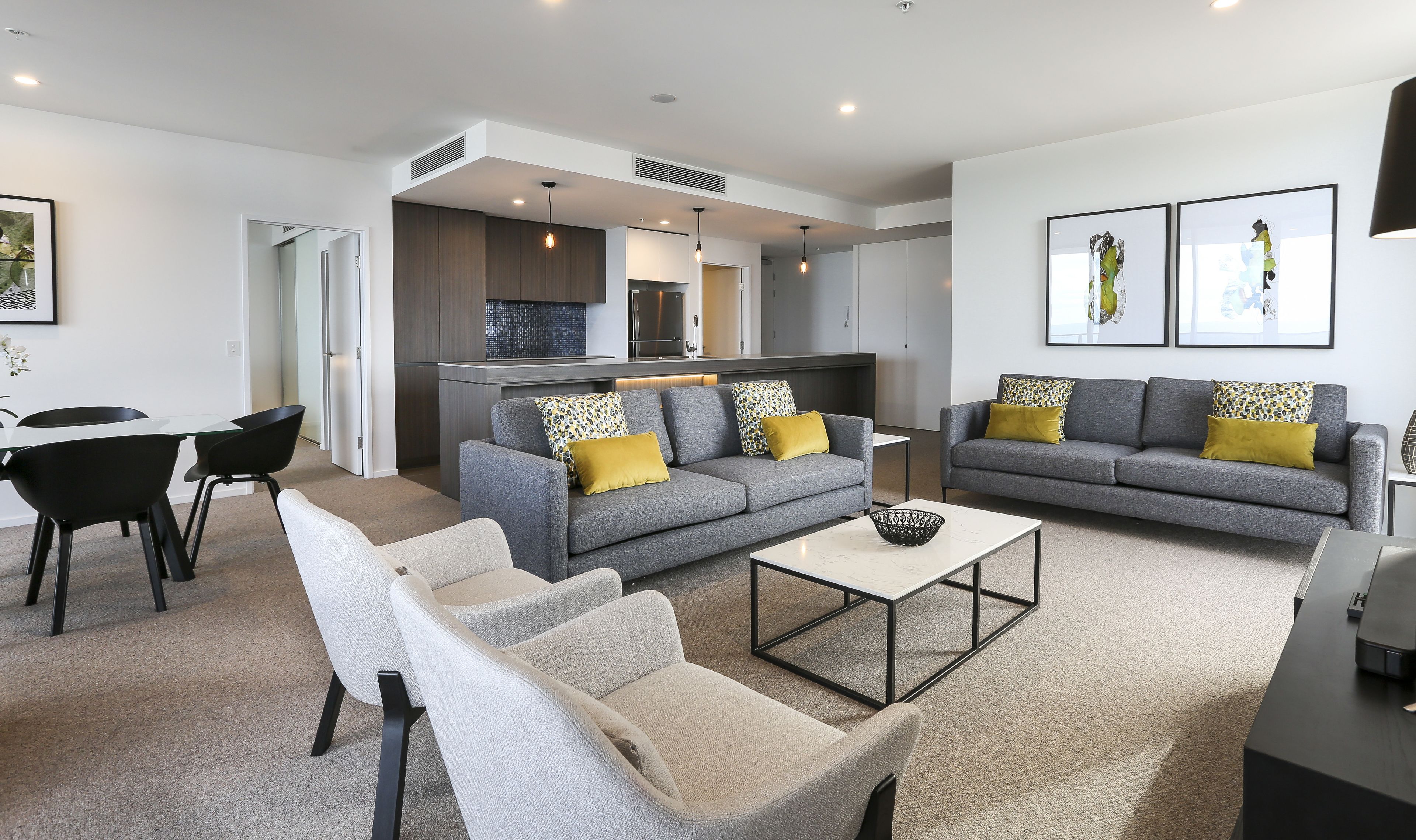 A modern living room with grey sofas, a coffee table, and a dining area with a glass table and black chairs.