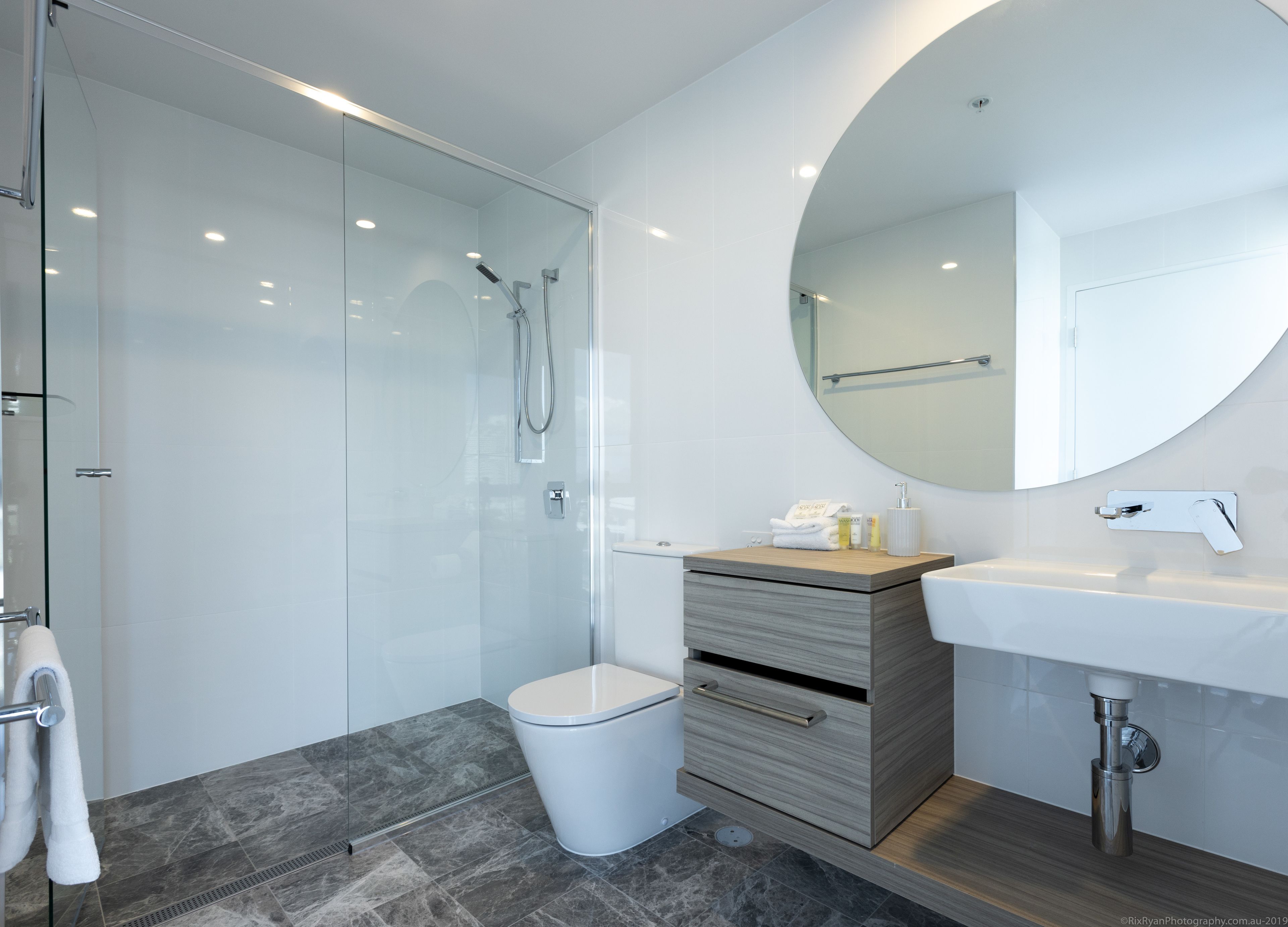 A modern bathroom with a glass-enclosed shower, a wooden vanity with a sink, and a large mirror.