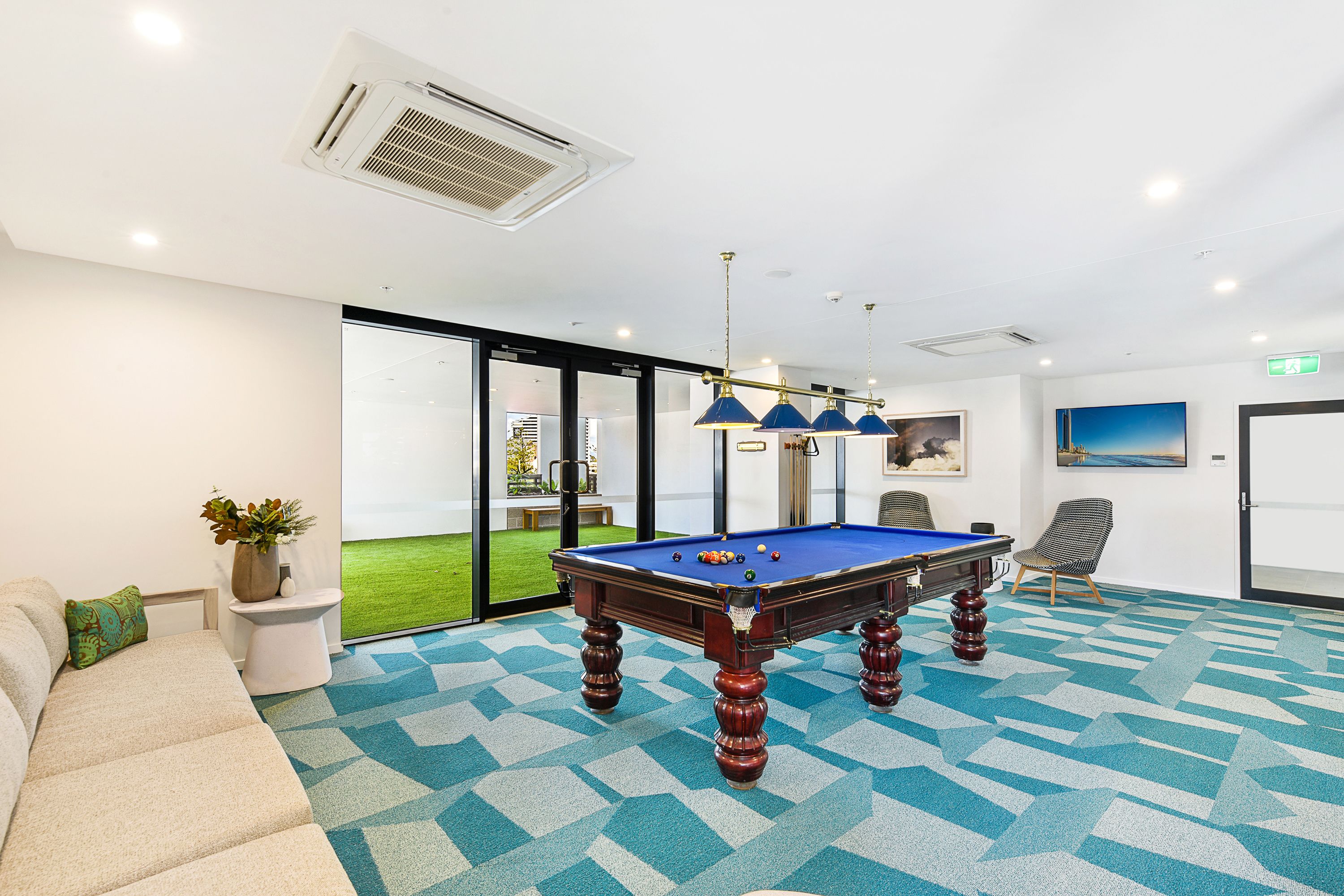 A pool table in a room with a geometric carpet, a sofa, and a chair.