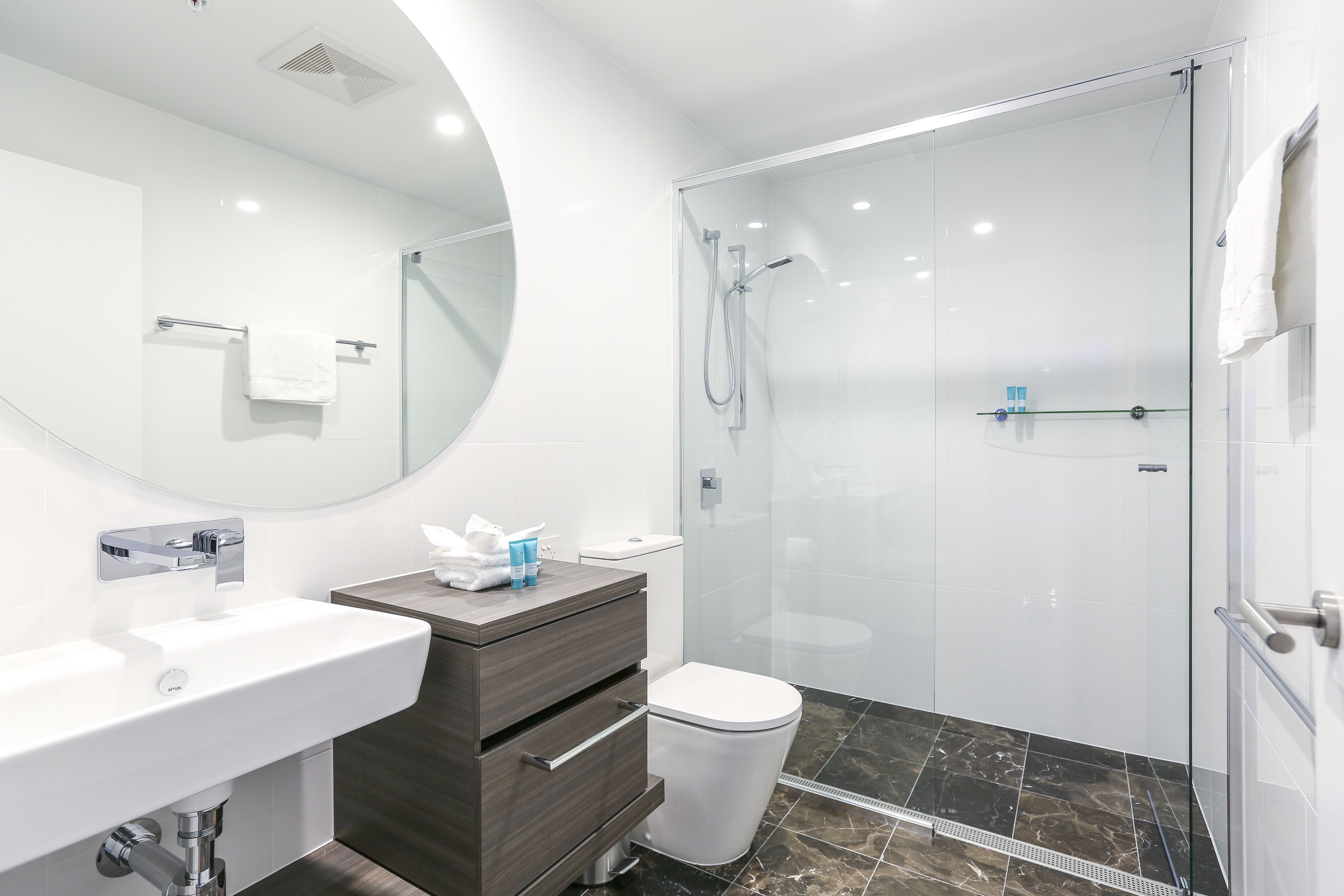 A modern bathroom with a glass-enclosed shower, a white sink, and a vanity with drawers.