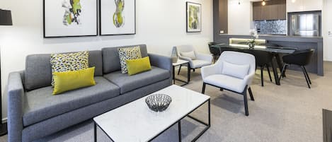 A modern living room with a grey sofa, a white coffee table, and a dining area with a kitchen in the background.