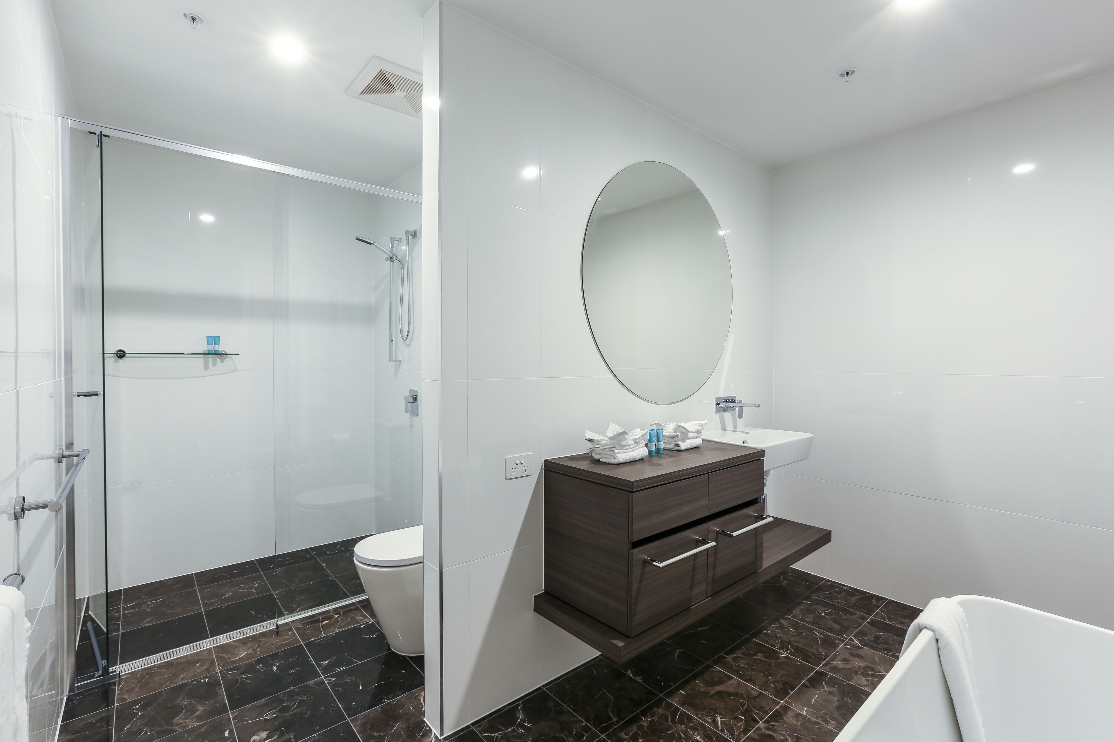 A modern bathroom with a glass shower enclosure, a dark wood vanity, and a large oval mirror.