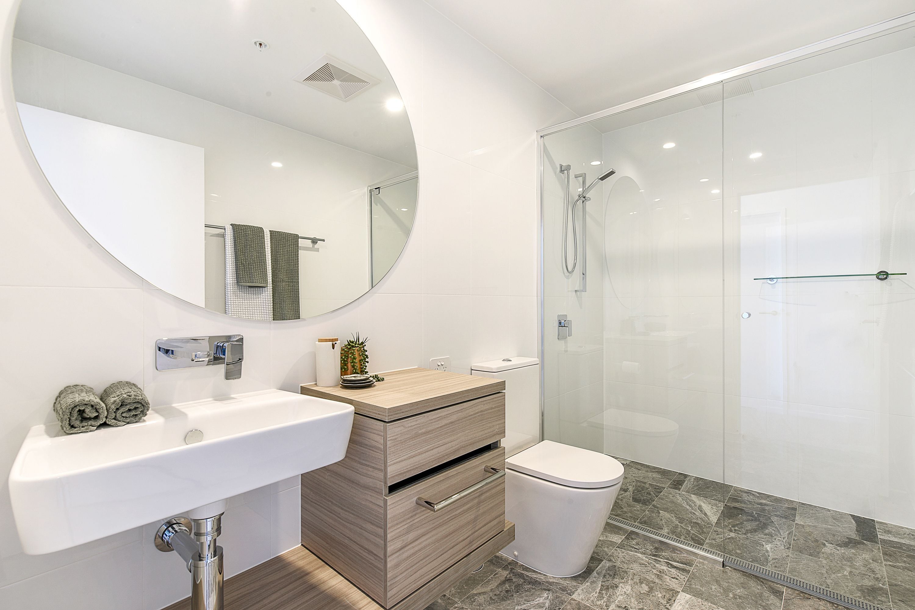 A modern bathroom with a round mirror, a sink, a toilet, and a glass-enclosed shower area.