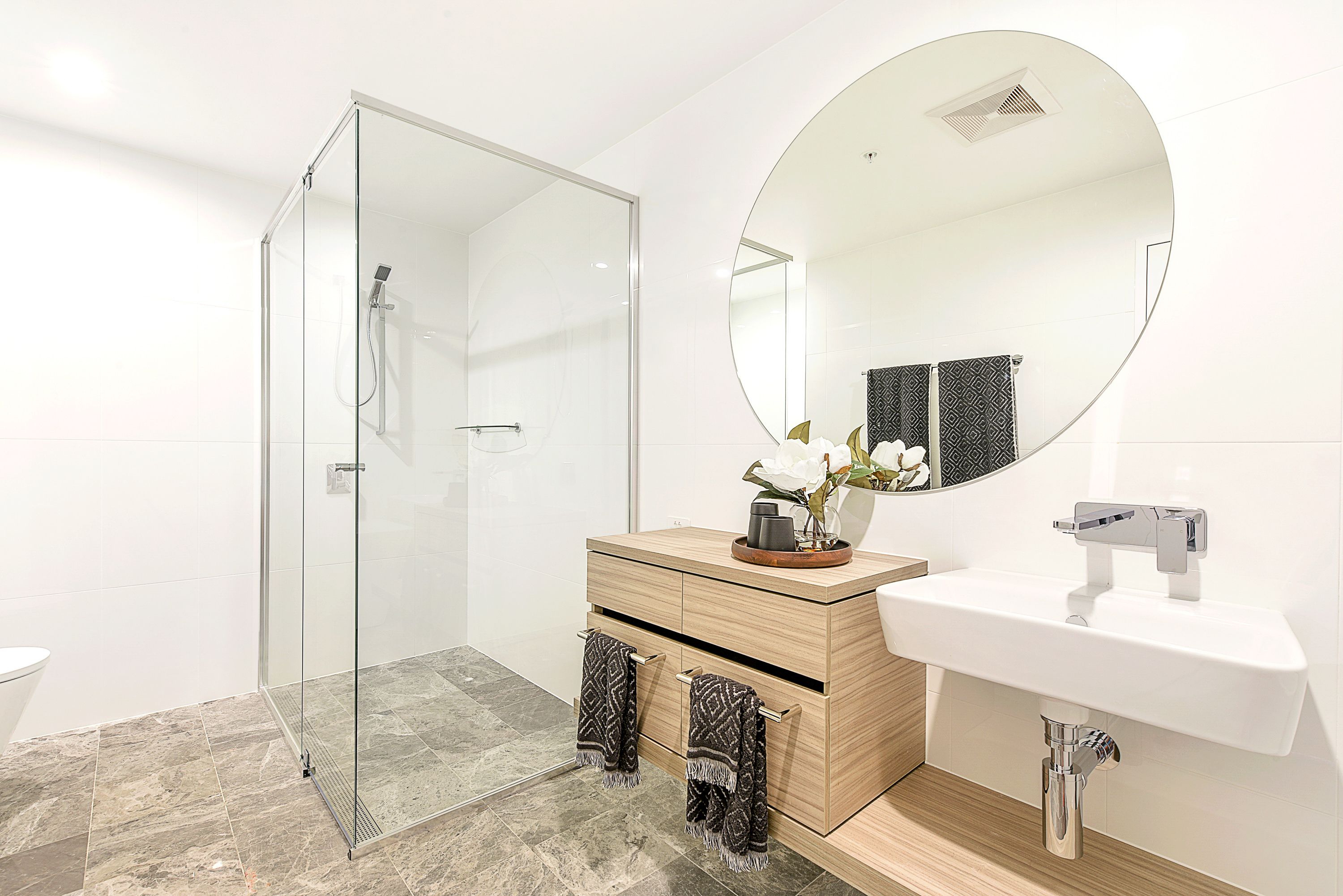 A modern bathroom with a glass-enclosed shower, a wooden vanity with a sink, and a large mirror.