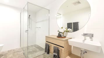 A modern bathroom with a glass-enclosed shower, a wooden vanity with a sink, and a large mirror.