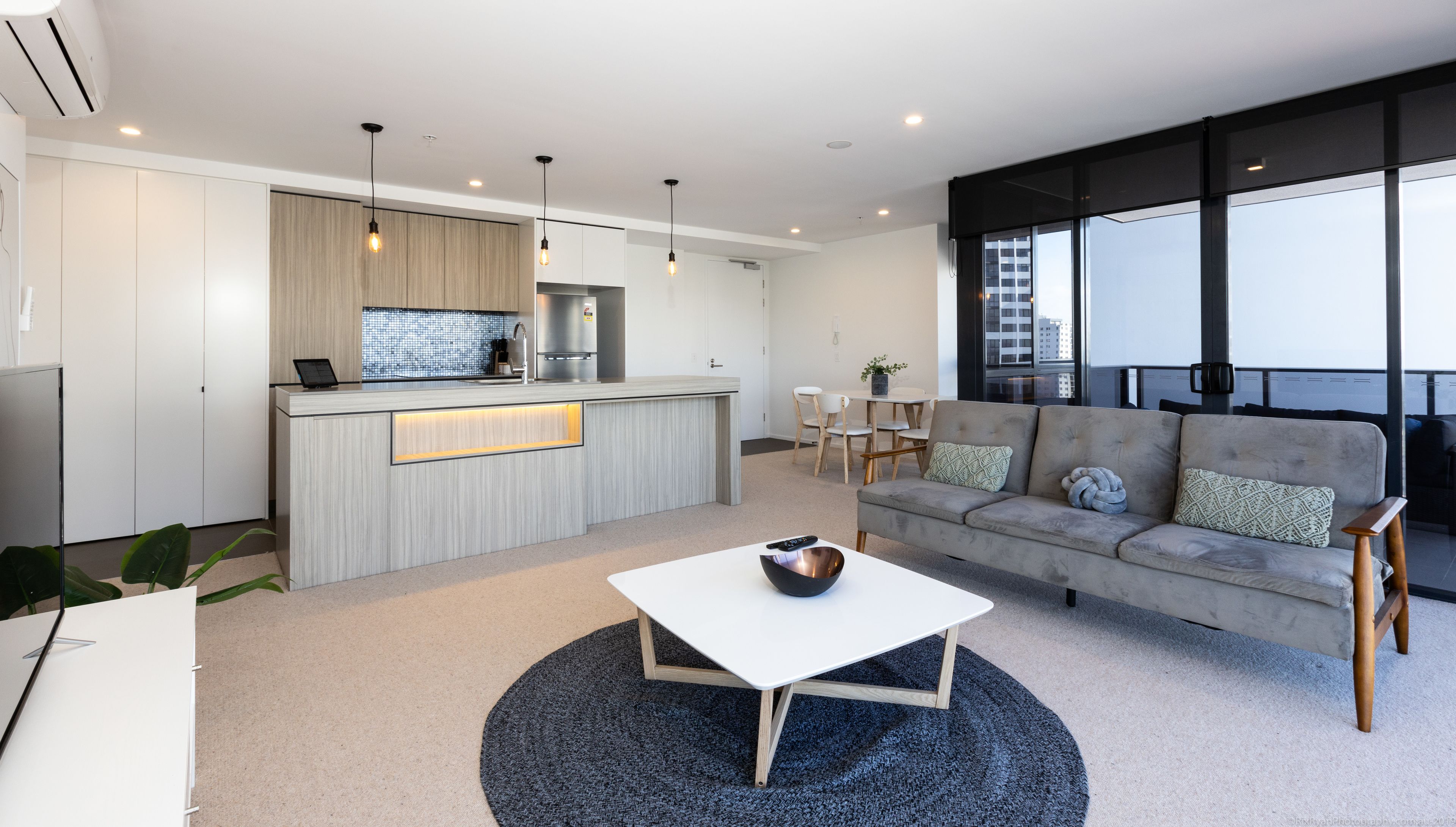 A modern living room with a sofa, a coffee table, and a kitchen area with a countertop and cabinets.