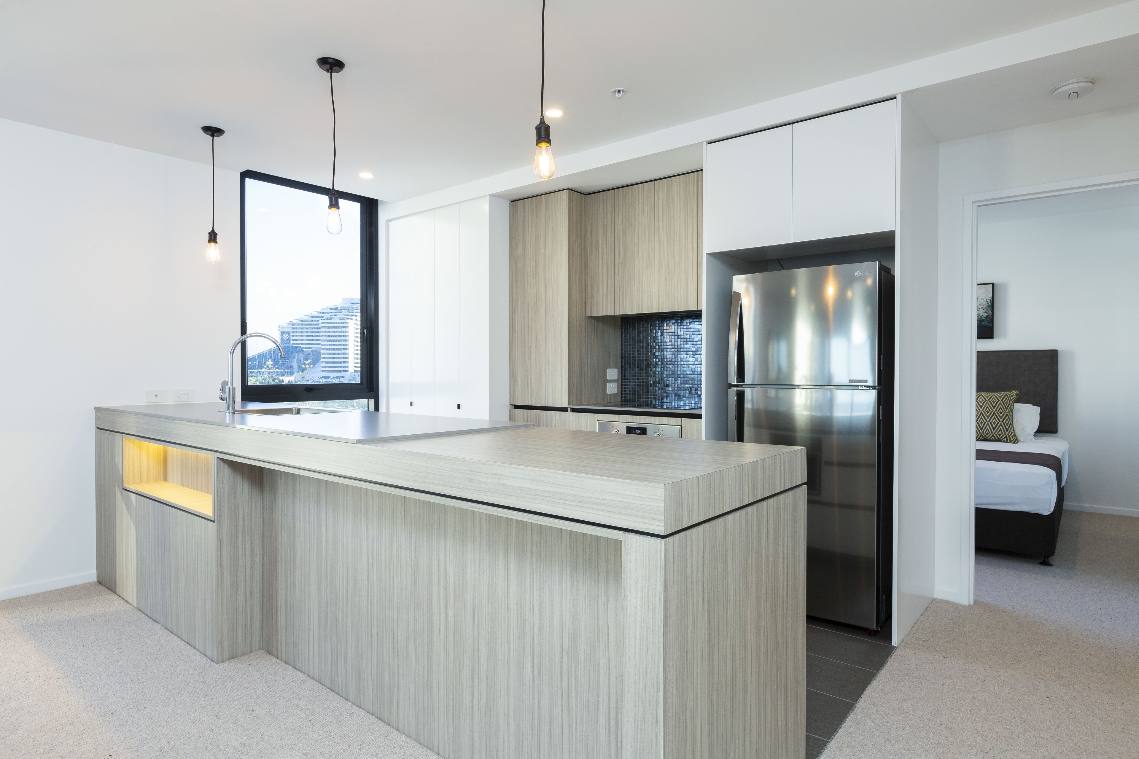 Una cocina moderna con una isla central, electrodomésticos integrados e iluminación colgante.