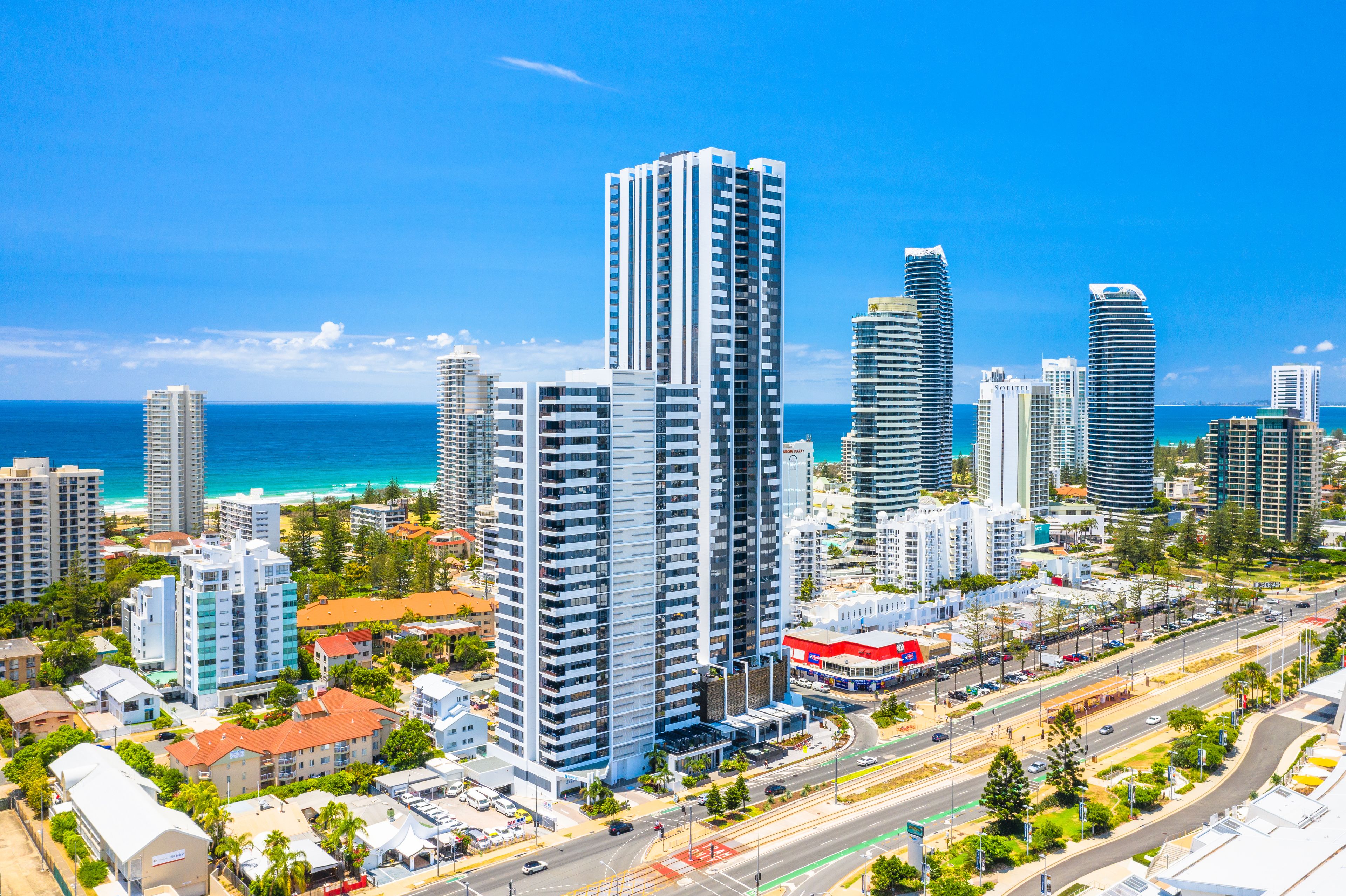A cityscape with high-rise buildings, a coastal view, and a busy road with vehicles.