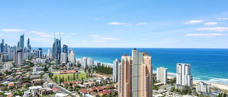 A coastal cityscape with high-rise buildings, a beach, and a clear blue sky.
