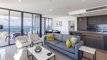 Una sala de estar moderna con un sofá gris, dos sillones, una mesa de centro y vistas al océano a través de amplios ventanales.