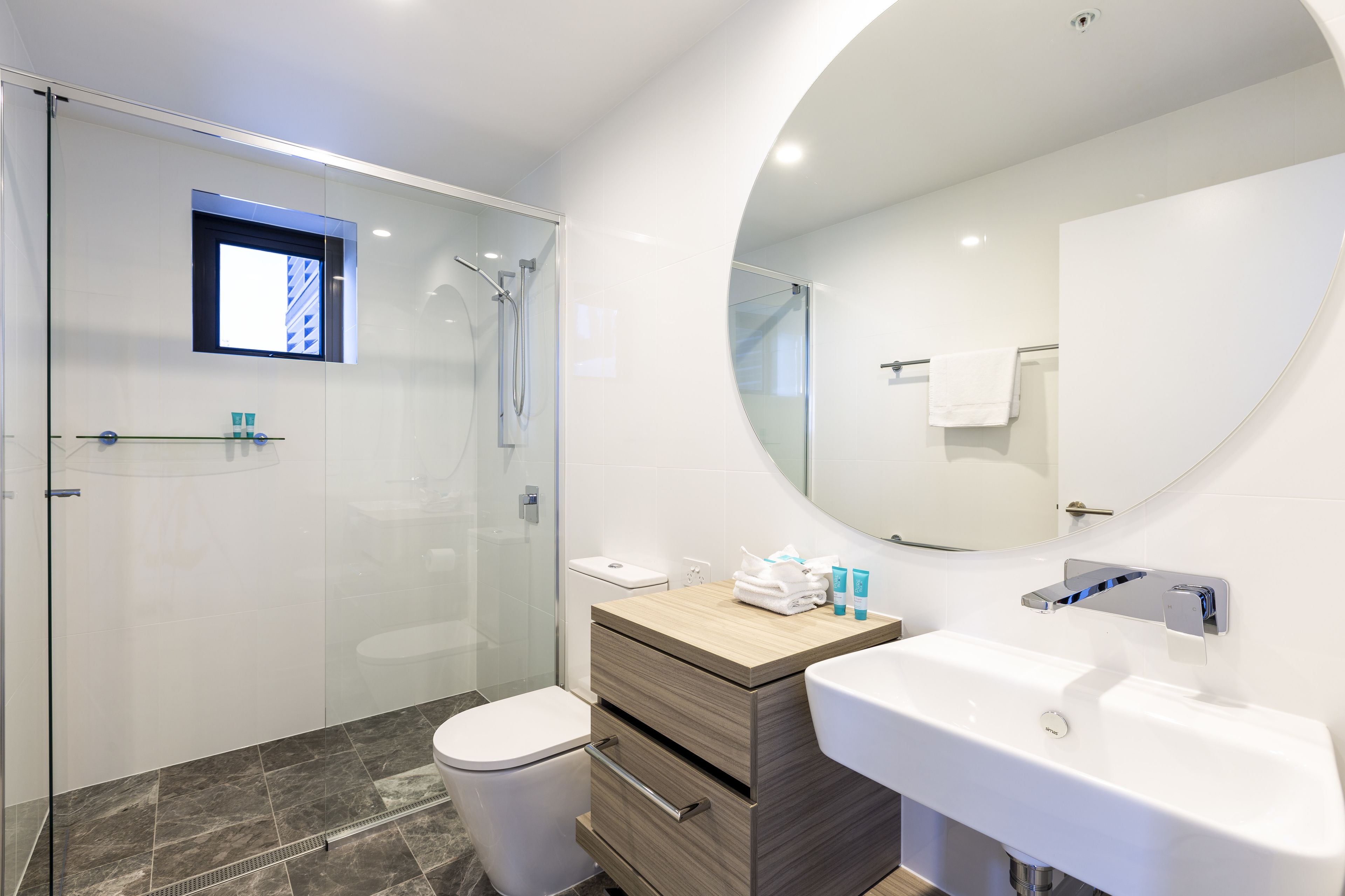 Un baño moderno con ducha de vidrio, tocador de madera con lavamanos y un espejo grande.
