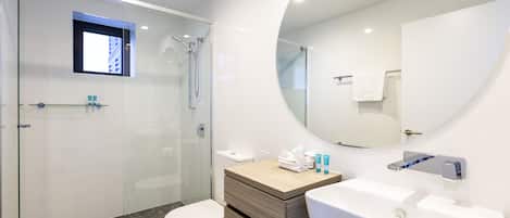 Un baño moderno con ducha de vidrio, tocador de madera con lavamanos y un espejo grande.