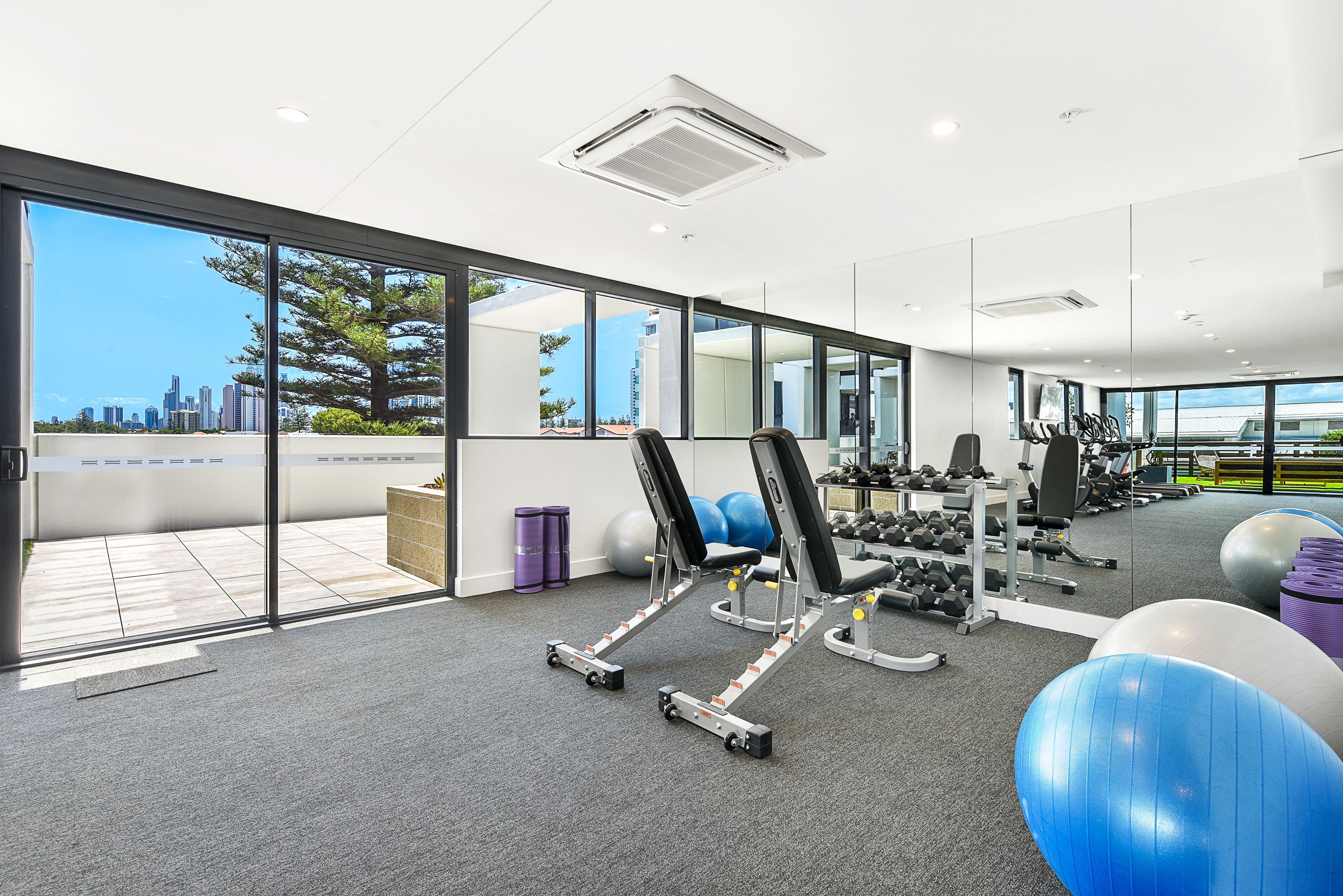 Un gimnasio moderno con equipo de ejercicio, ventanas amplias y vistas a la ciudad.