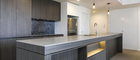 A modern kitchen with a large island, dark wood cabinetry, a stainless steel refrigerator, and pendant lighting.