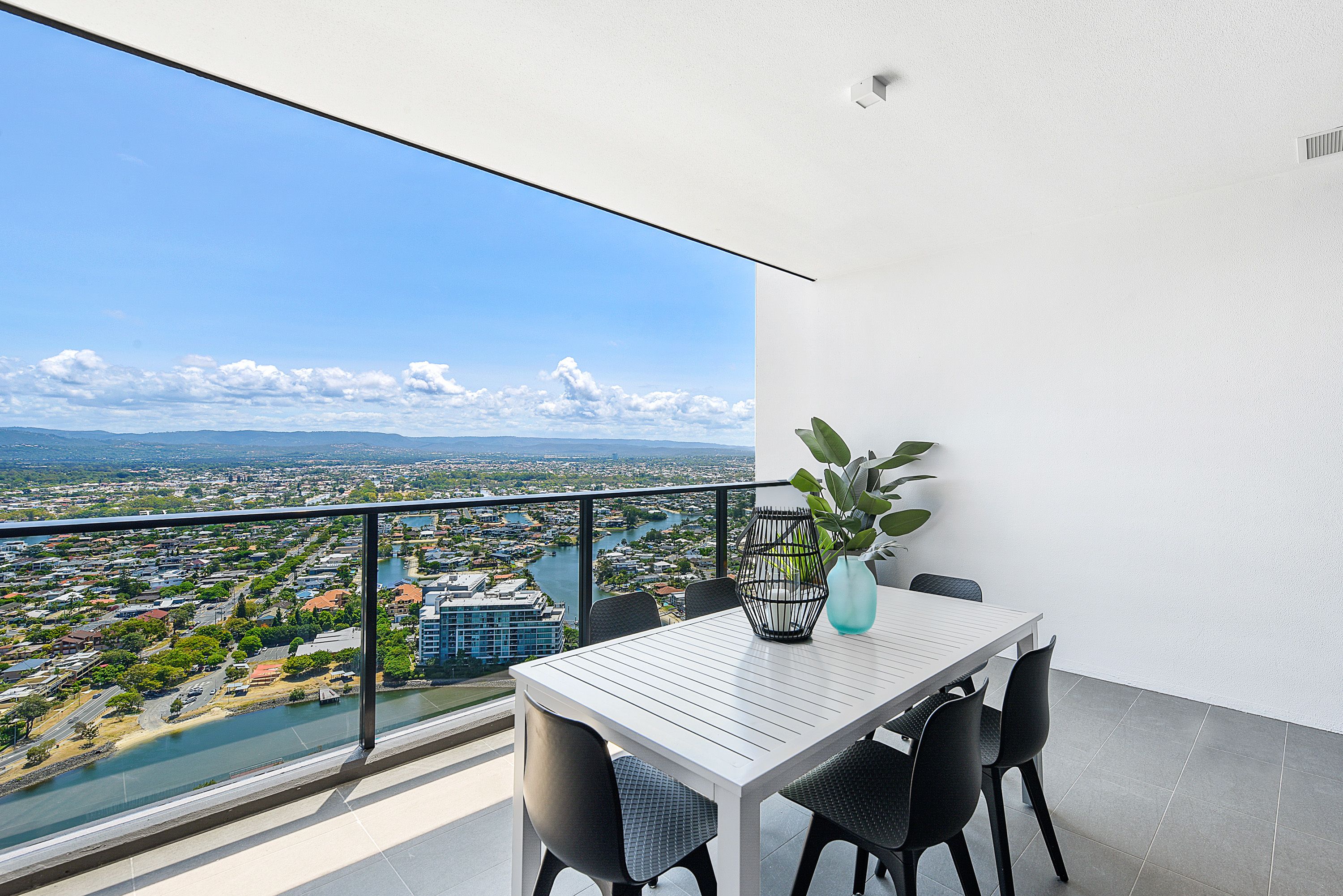 Un balcon avec une table et des chaises blanches, un pot de fleurs et une vue sur le paysage urbain et la rivière.
