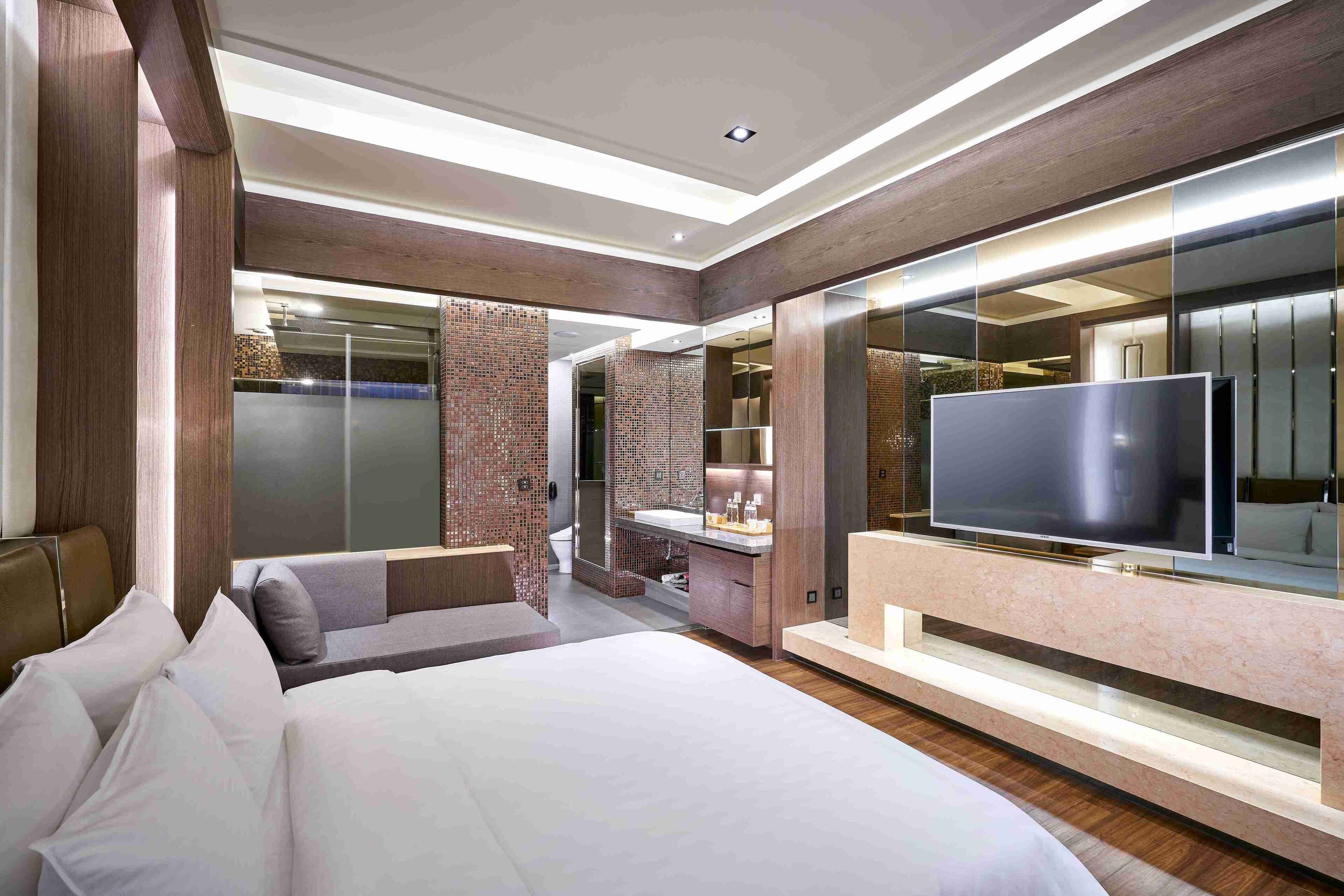 A modern hotel room with a large bed, a TV, and a bathroom with a mirror and sink.