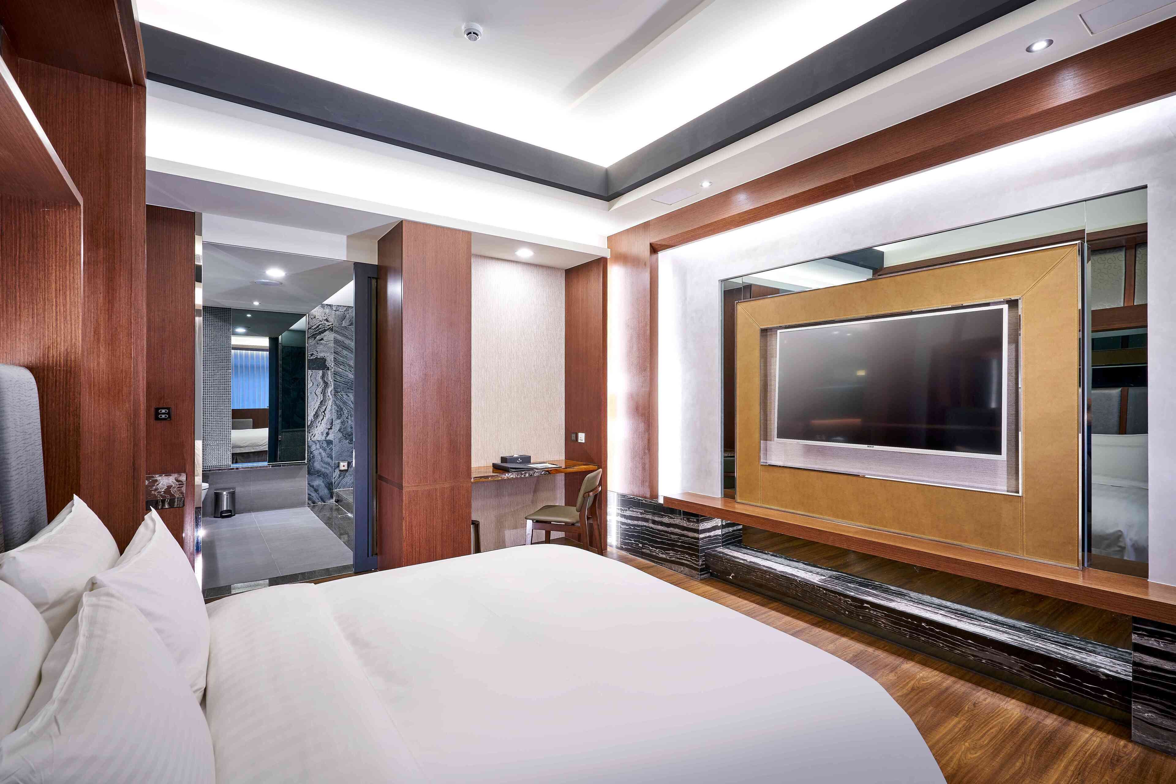 A modern hotel room with a large bed, a TV mounted on the wall, and a desk with a chair.