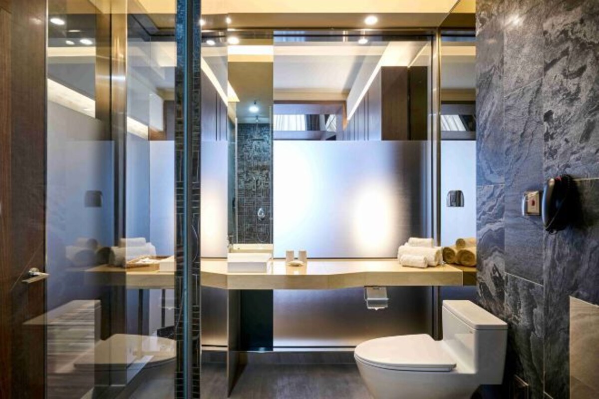 Une salle de bain moderne avec une cloison en verre, un mur en marbre et des toilettes blanches.