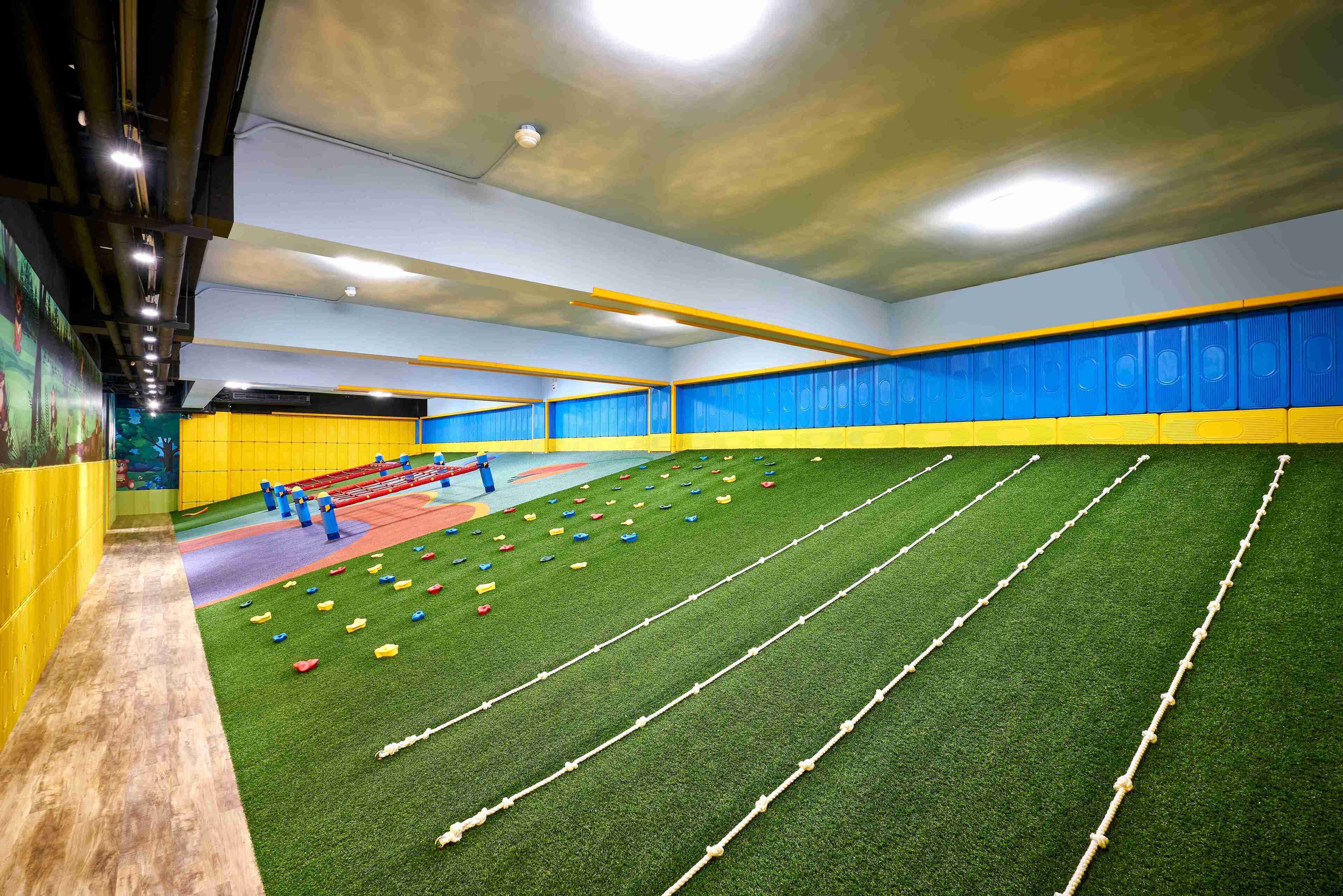 An indoor sports facility with artificial turf, exercise equipment, and a climbing wall.