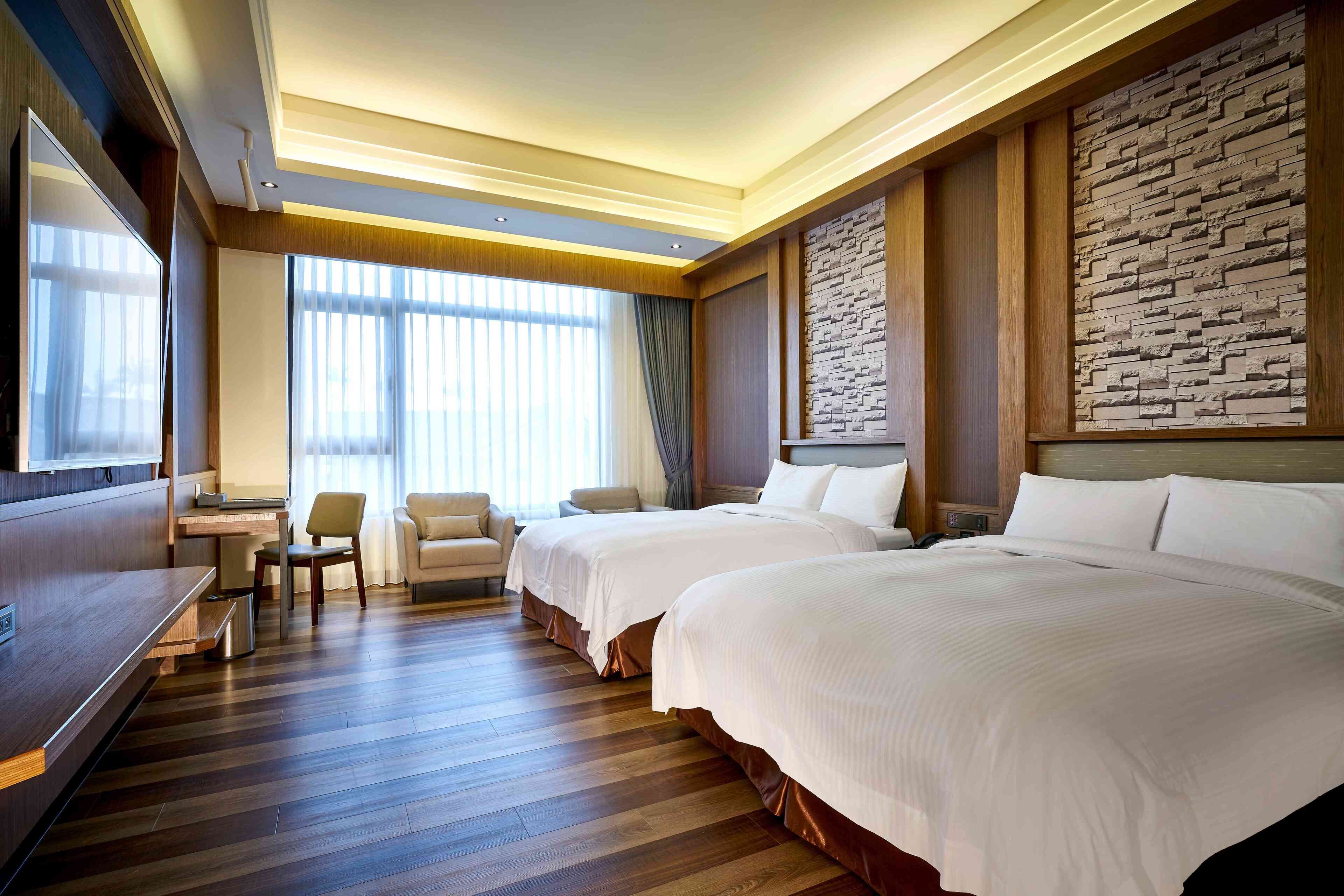 A hotel room with two beds, a desk, a chair, and a large window with curtains.