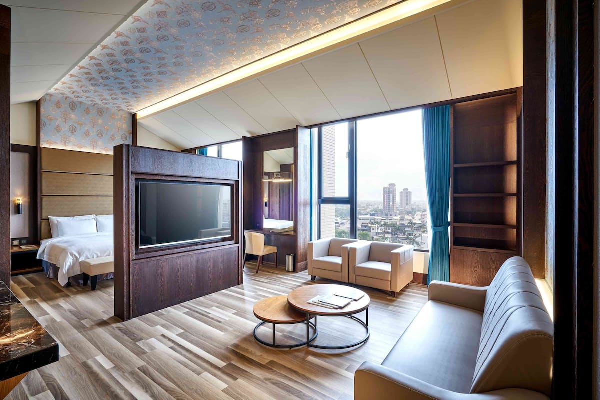 A modern hotel room with a large bed, a TV, a sofa, and a coffee table.
