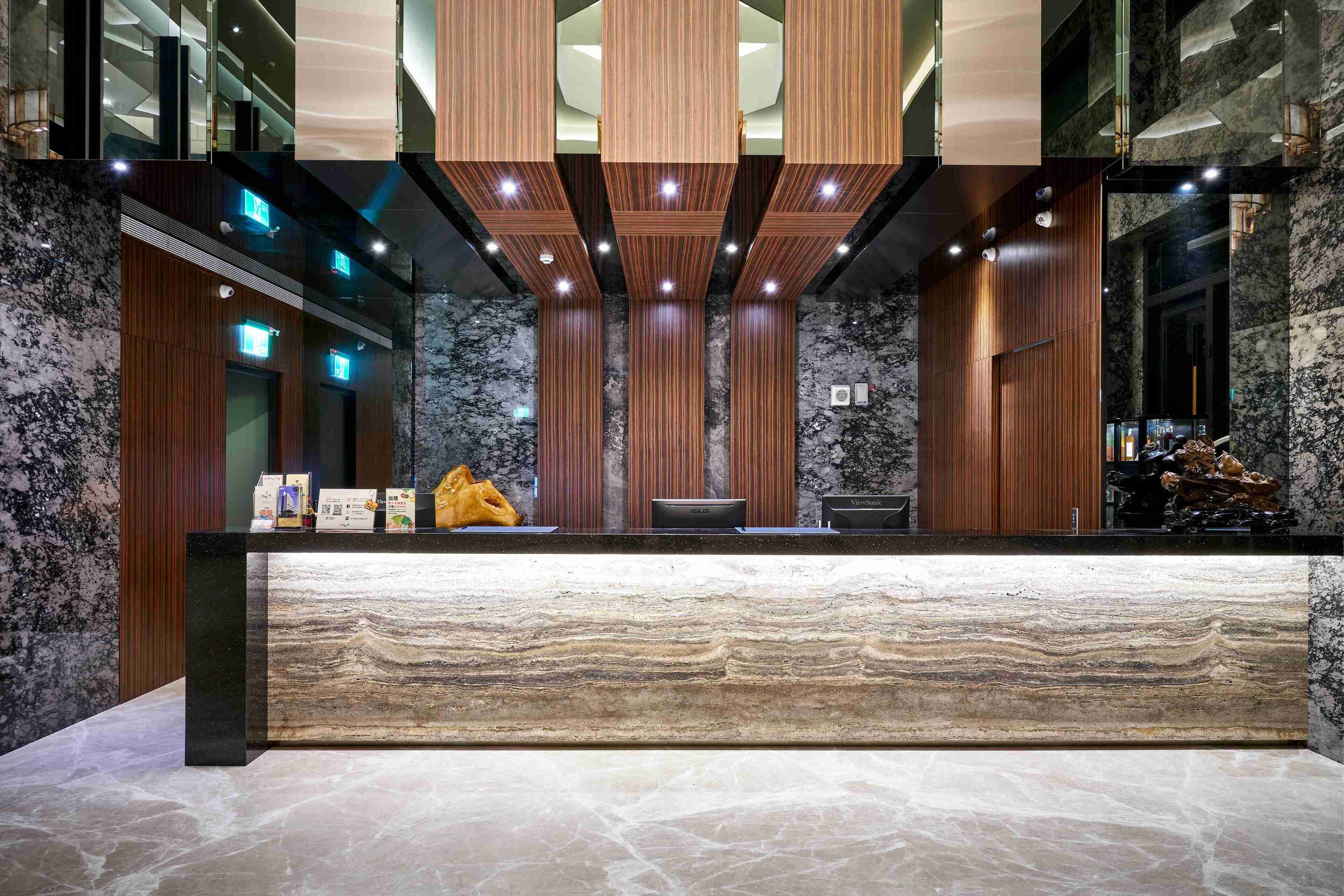 Un mostrador de recepción con encimera de mármol, paneles verticales de madera y un diseño de techo moderno con iluminación empotrada.