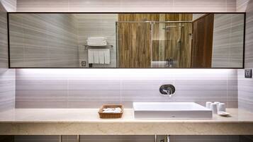 A modern bathroom with a large mirror, a sink with a marble countertop, and a shower area with wooden panels.