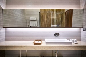 A modern bathroom with a large mirror, a sink with a marble countertop, and a shower area with wooden panels.