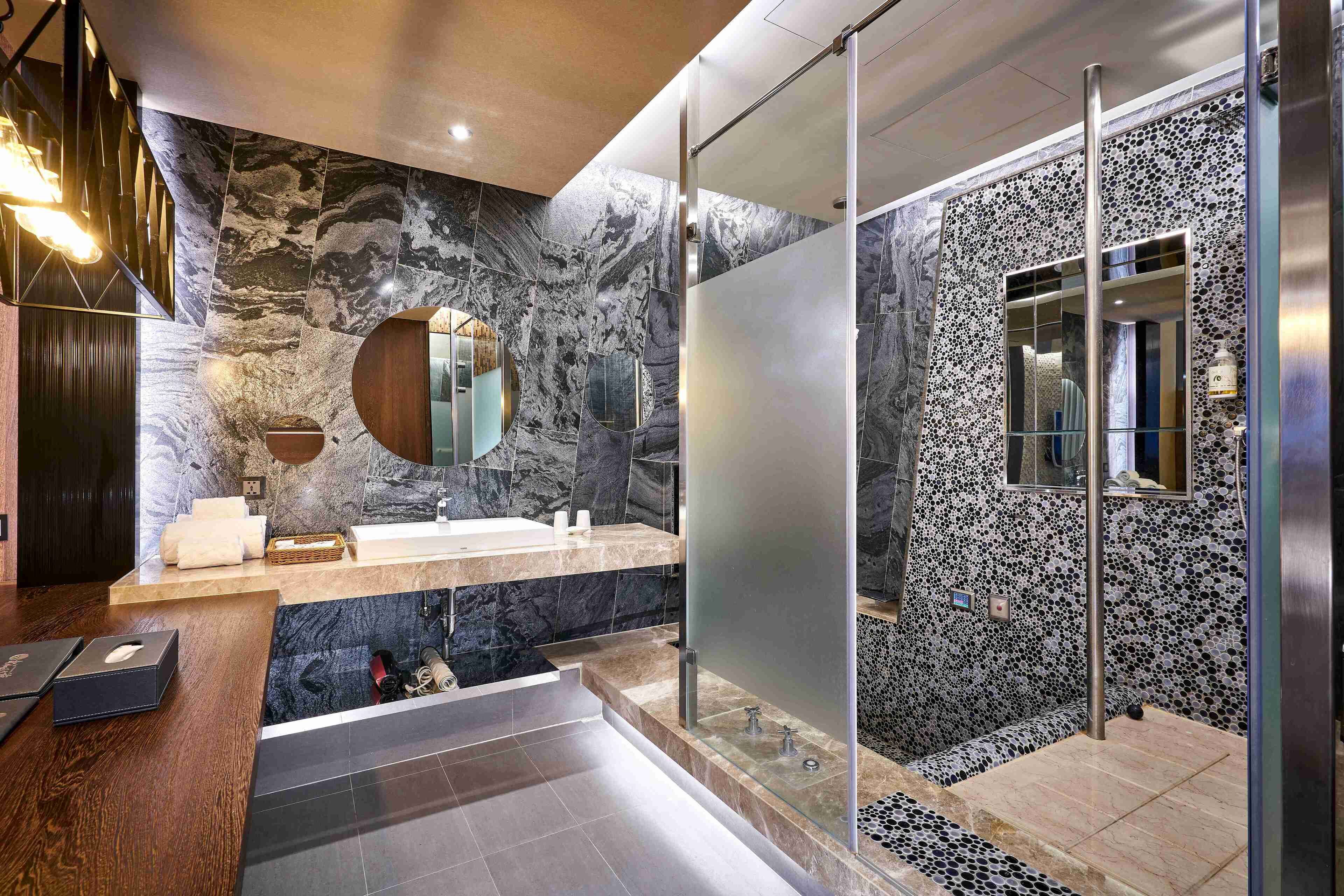 Un baño moderno con pared de mármol, cabina de ducha de vidrio y tocador de madera.