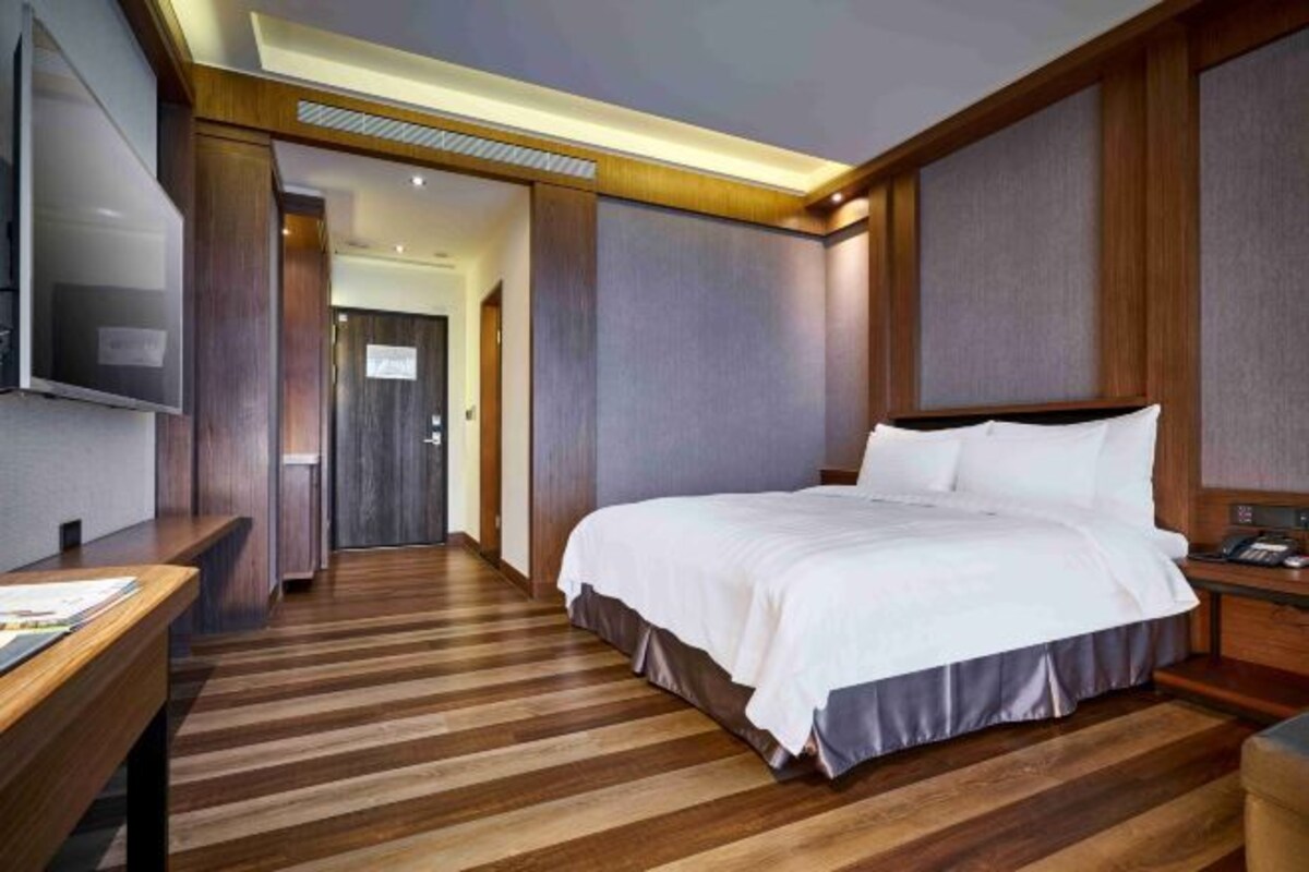 Une chambre d’hôtel avec un grand lit, un bureau, un téléviseur à écran plat et un plancher en bois.
