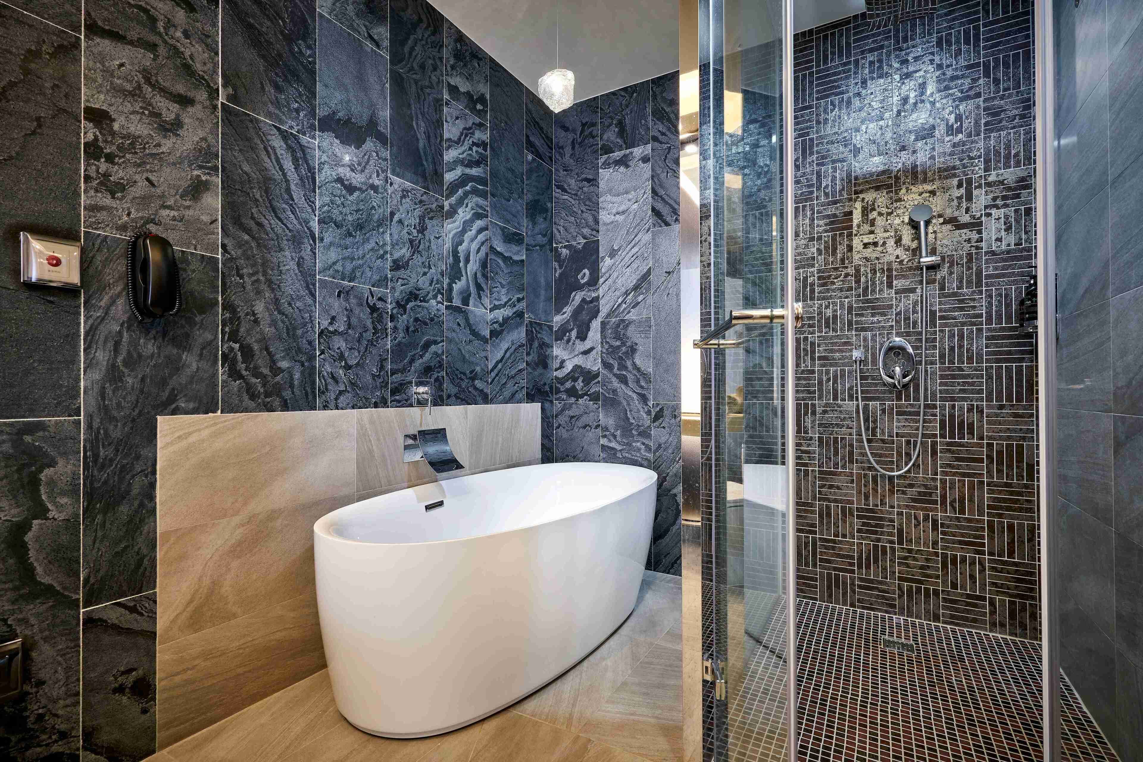 A modern bathroom with a freestanding bathtub, a glass-enclosed shower, and a marble-tiled wall.