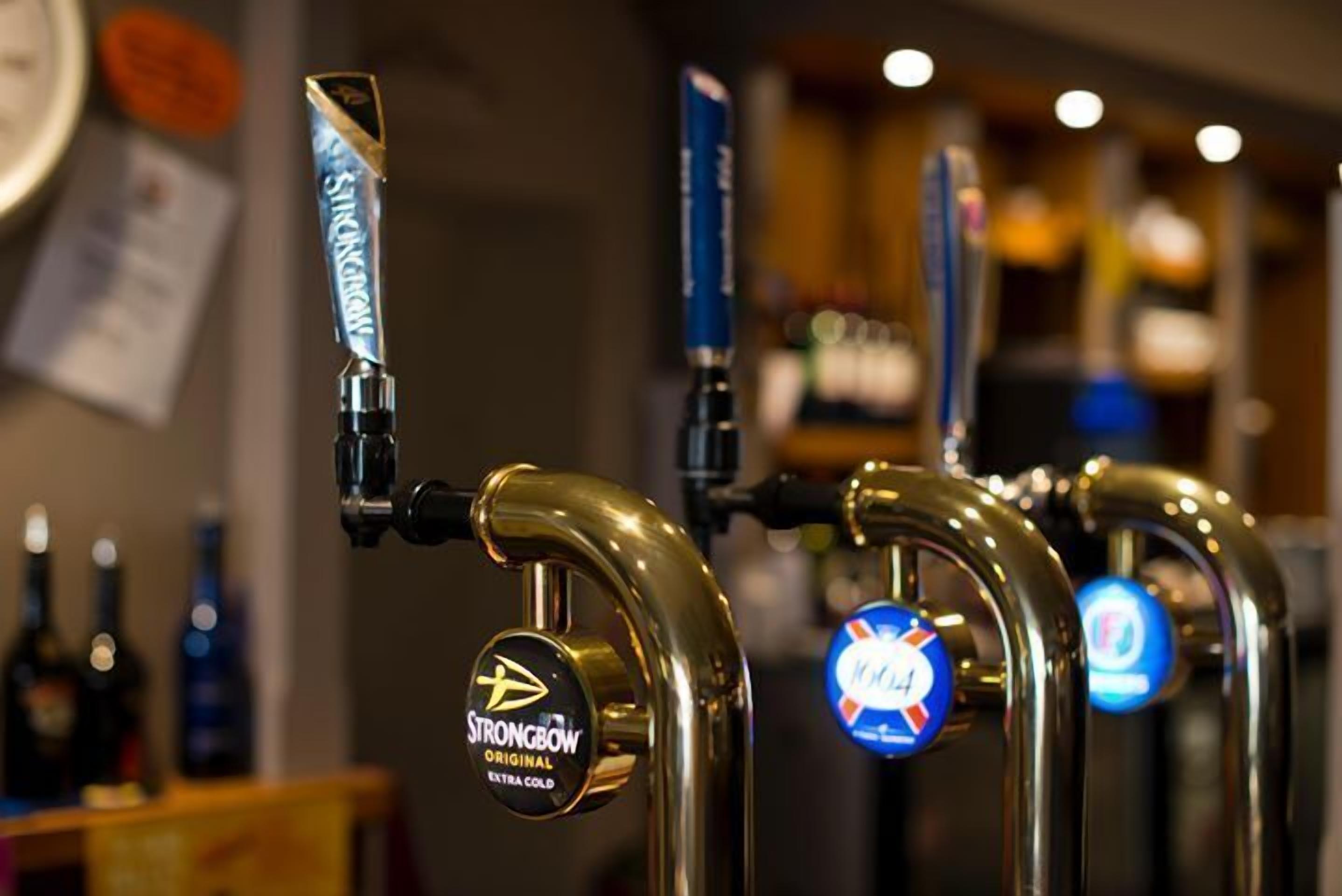 Une rangée de robinets à bière, chacun portant une étiquette, dont un pour la bière Strongbow Original Extra Cold.