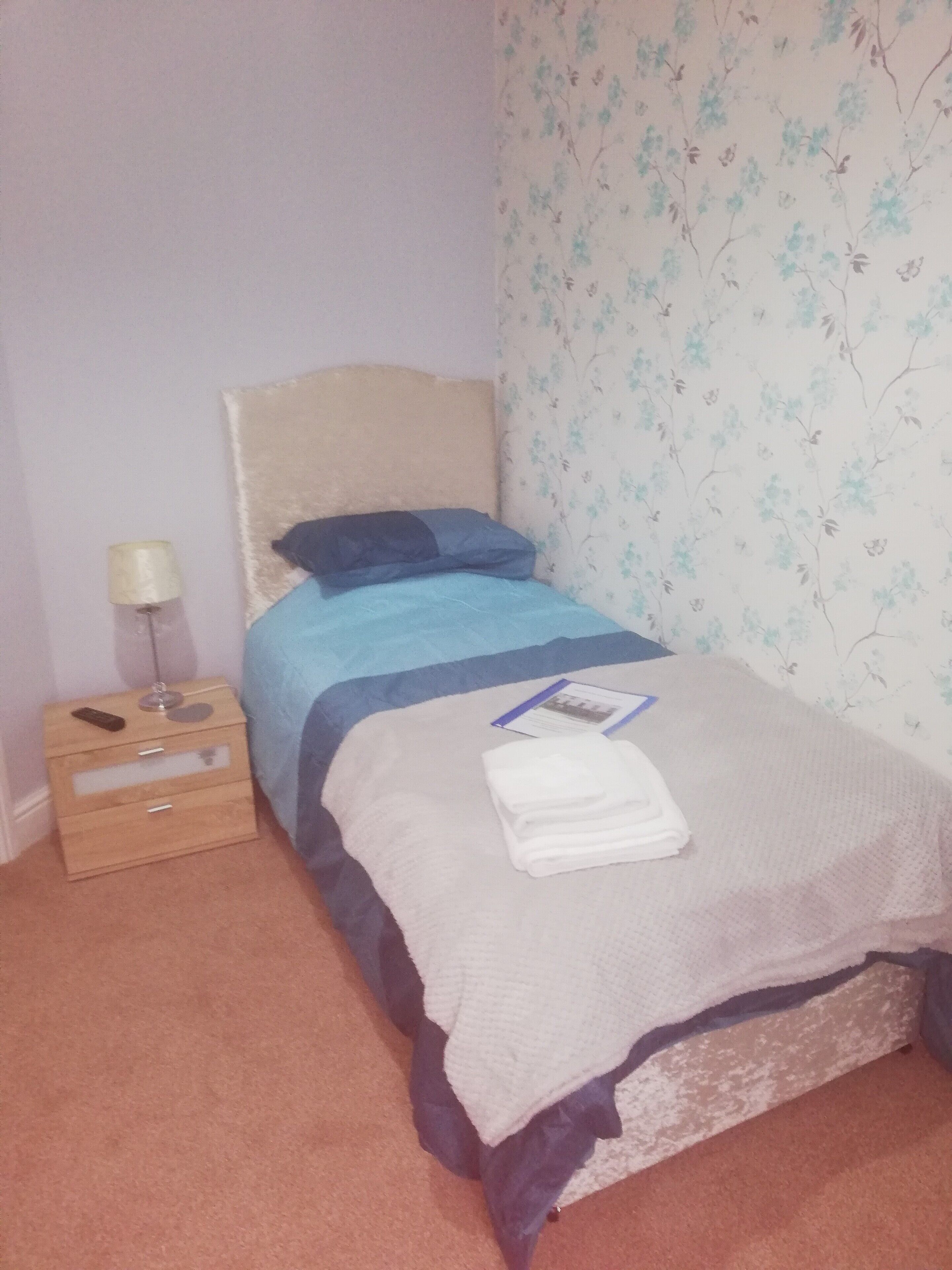 Un dormitorio con cama, mesita de noche, lámpara y papel tapiz floral.
