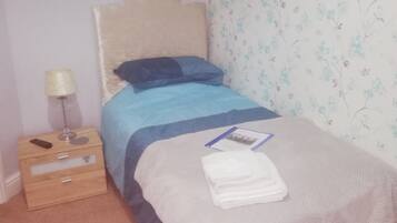 Un dormitorio con cama, mesita de noche, lámpara y papel tapiz floral.