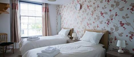 Une chambre d’hôtel avec deux lits, une chaise, une table de chevet avec une lampe et une fenêtre avec des rideaux.