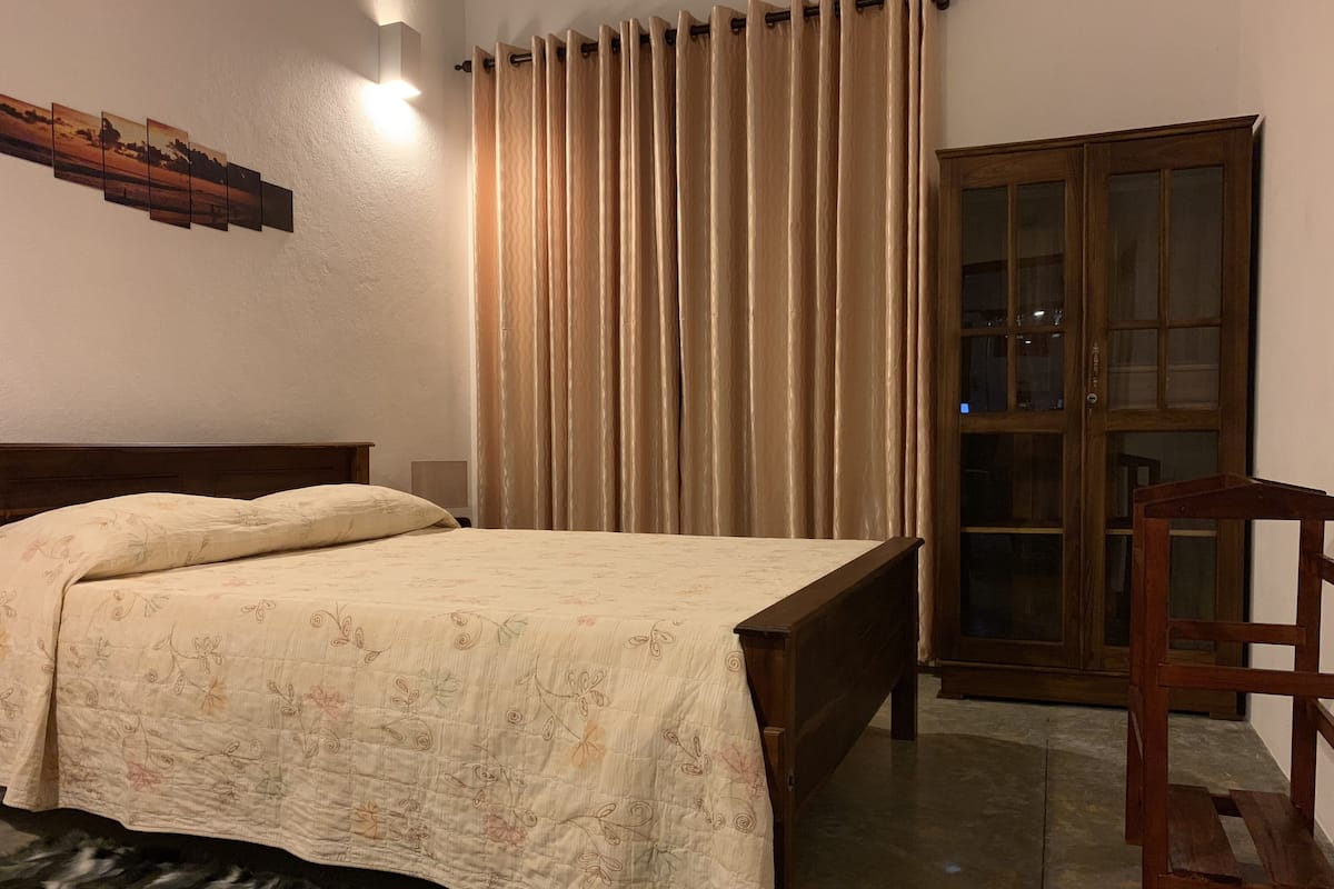 A bedroom with a bed, curtains, a wooden chair, and a cabinet.