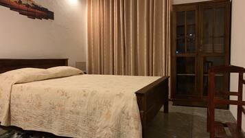 A bedroom with a bed, curtains, a wooden chair, and a cabinet.