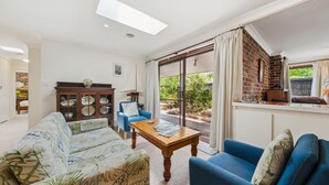 A spacious living room with a blue sofa, a wooden coffee table, and a cabinet with glass doors. - Rosella Retreat | Perfect getaway for family and friends (Blackheath)